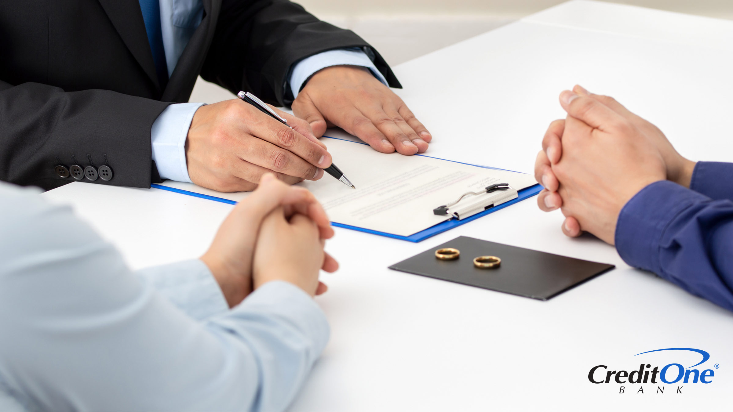 A lawyer reviews paperwork at a negotiation table as a man and woman sit at adjacent corners, a scene that may occur during divorce proceedings while determining who is responsible for credit card debt.