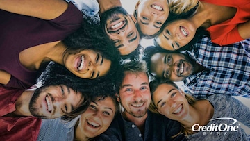 A diverse friend group of millennials gathers in a huddle, smiling happily while considering how credit scores affect their social status.