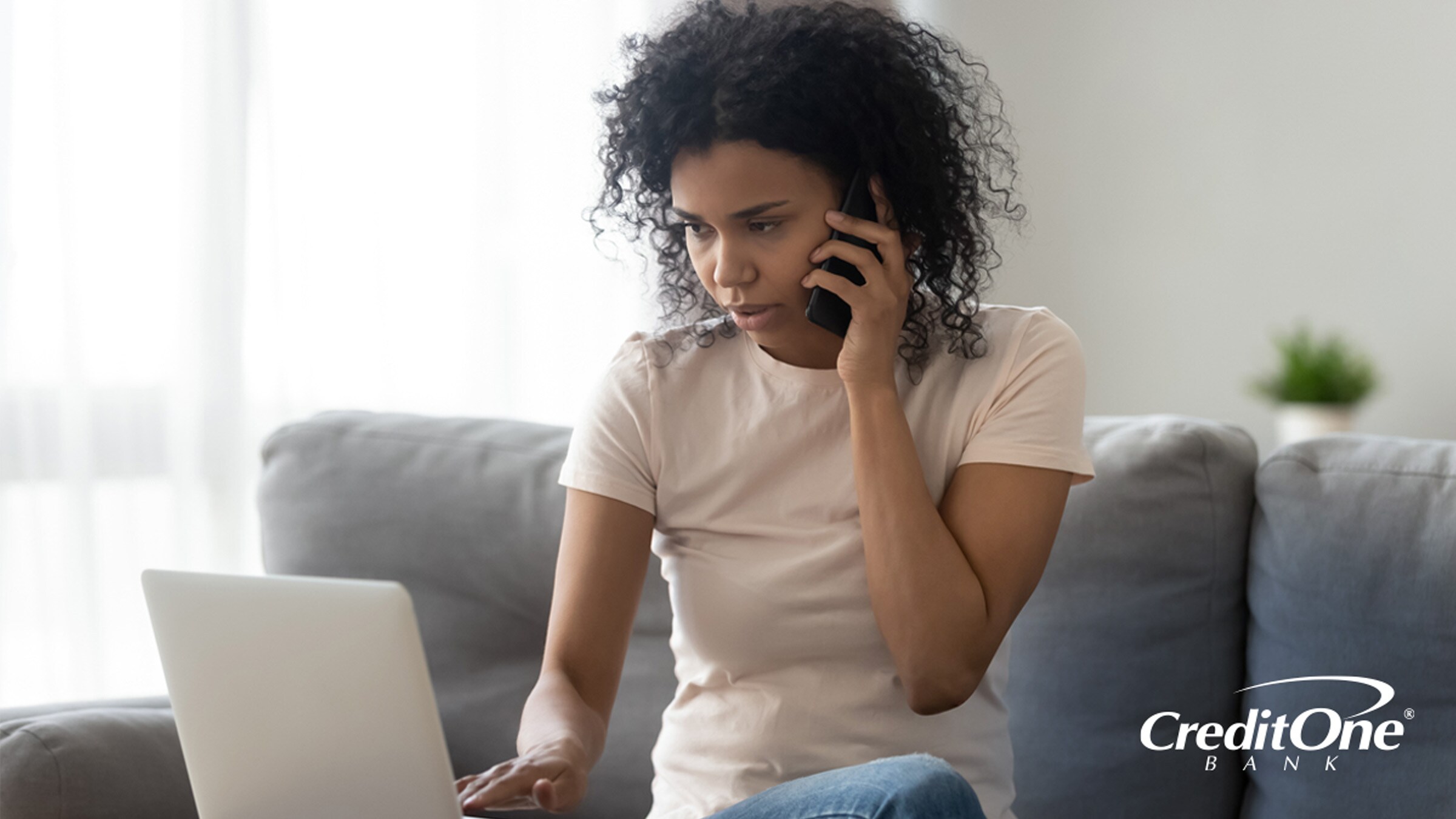 A woman looks at her laptop with a concerned expression as she talks on the phone, possibly trying to deal with a missing credit card payment. 