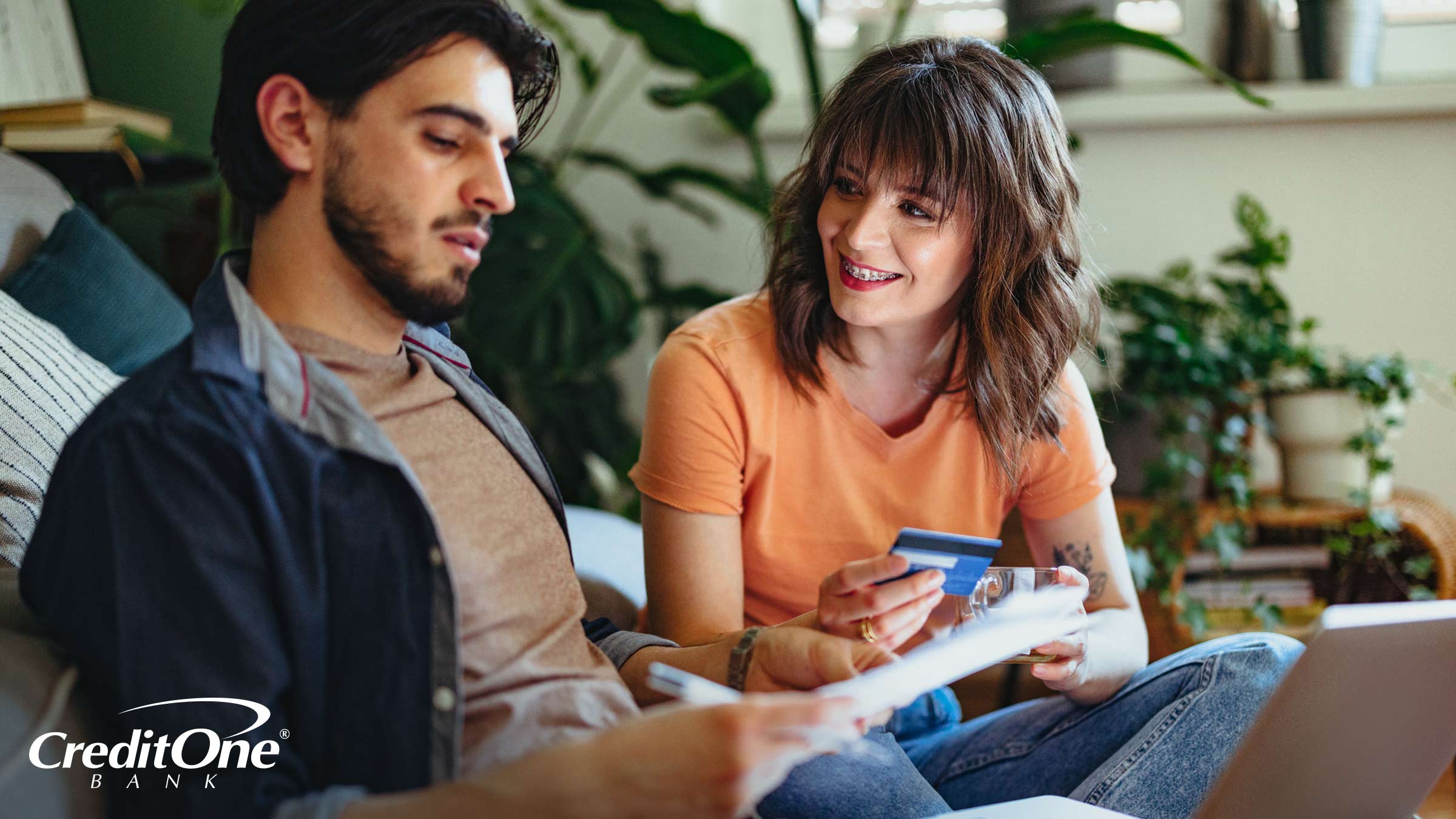 A young couple holds a credit card while checking their paperwork, possibly trying to find out the terms of their credit card insurance protection.