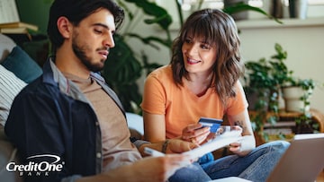 A young couple holds a credit card while checking their paperwork, possibly trying to find out the terms of their credit card insurance protection.