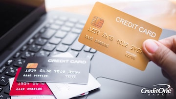 A hand holds a credit card while a pile of several more sits on a laptop keyboard, indicating that the cardholder has often applied for credit cards.