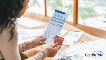 A young woman looks at her credit card and several past-due invoices, indicating her credit card may be charged off.