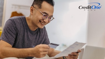 A man holds a credit card in one hand as he reviews a document he’s holding in the other. He is smiling, perhaps because this is the first step he’s taking toward rebuilding his credit with credit cards.