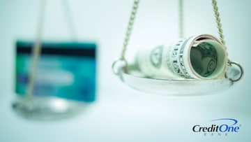 A credit card and roll of cash balance against each other on a set of scales, representing a balance transfer of money from one card to another.