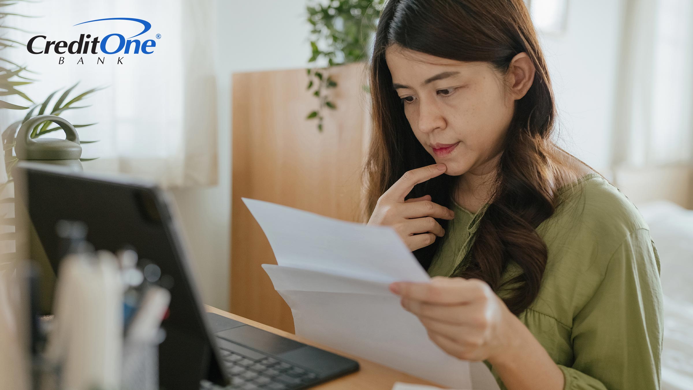 A woman inspects a few documents while working at her computer desk. Perhaps she’s comparing her credit scores from FICO and VantageScore while applying for credit.