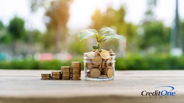 Four increasingly tall stacks of coins are set beside a jar, which is also filled with coins and has a small plant sprouting from it. This represents the act of investing and growing wealth.